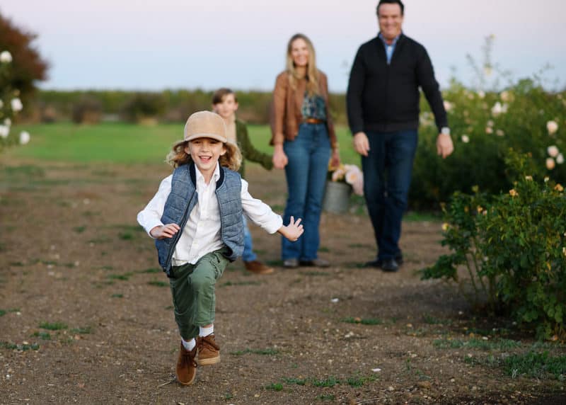 young boy running toward the photographer with family walking behind during fall family photos in yuba city california