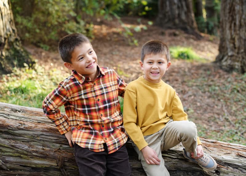 two young brothers sitting on a log and laughing together during fall family photos in davis california