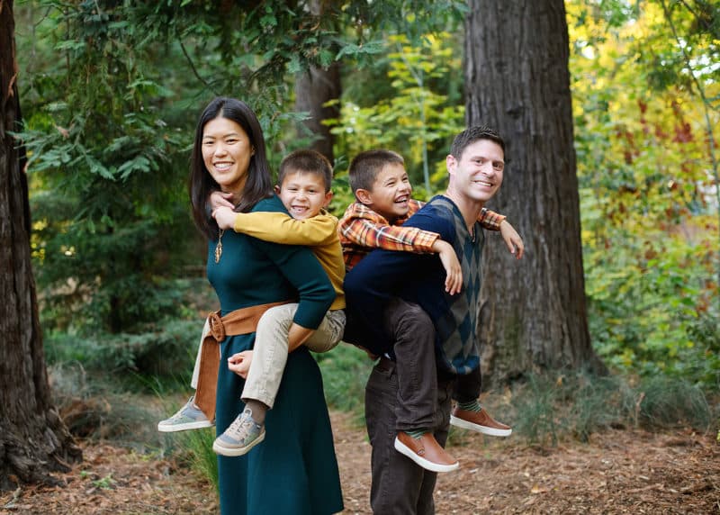 mom and dad holding sons on their backs and laughing together during family photo shoot with davis photographer jill carmel