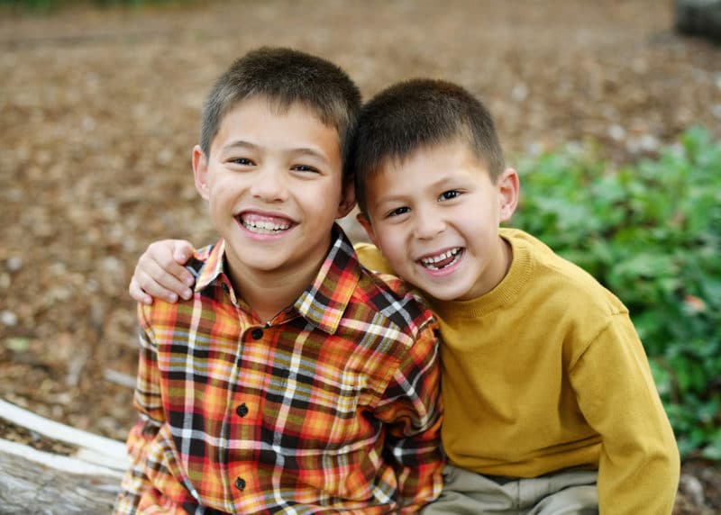 two young brothers sitting on a redwood log and smiling together during family photo session in davis california