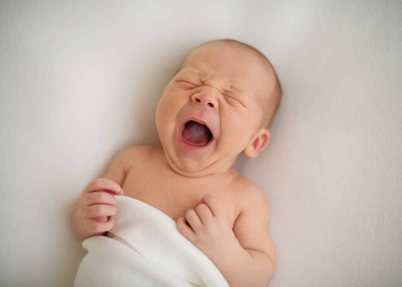 newborn baby yawning against a white blanket during newborn photo session with photographer jill carmel