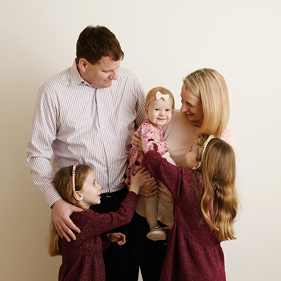 family of five standing against a studio wall and looking at one another during photo session