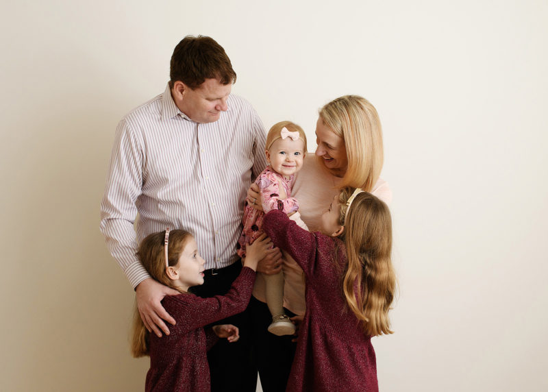 family of five standing against a studio wall and looking at one another during photo session 