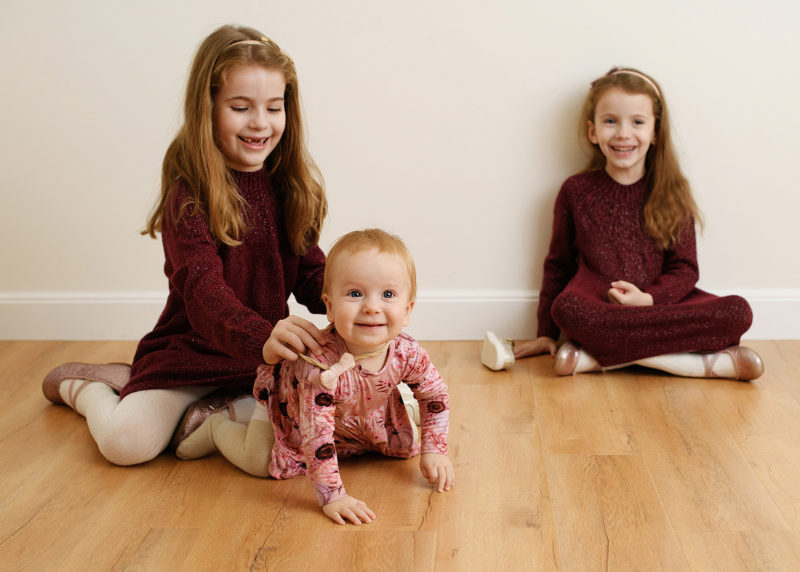 Young baby crawling while big sisters look on during studio session in sacramento california