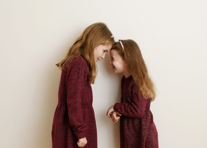 two sisters standing head to head and laughing at one another during family photo session in sacramento california