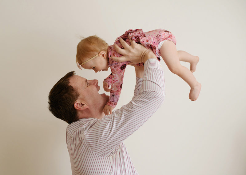 dad holding one year old baby girl in the air and smiling