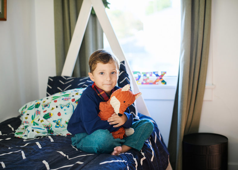 young boy hugging an orange fox toy while sitting on his bed during photo session in sacramento california