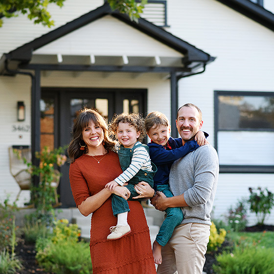 family of four standing in front of family home and smiling during photo session with sacramento photographer jill carmel