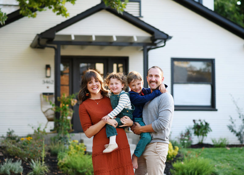 family of four standing in front of family home and smiling during photo session with sacramento photographer jill carmel